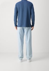 Granatowa koszula z długim rękawem i okrągłym dekoltem w połączeniu z jasnoniebieskimi dżinsami, o luźnym kroju i dwóch tylnych kieszeniach.