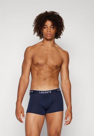Boxers en bleu marine avec un logo blanc Lacoste sur la ceinture élastique, fabriqués en tissu doux, présentant un design ajusté.