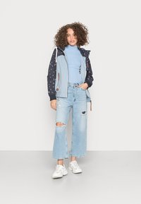 Casaco azul claro com capuz estampado de estrelas escuras, combinado com jeans azul claro de cintura alta e rasgados, e ténis brancos.