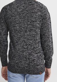 Black and grey marled knit sweater with long sleeves, ribbed cuffs and hemline, and a small branded tag at the back bottom left.
