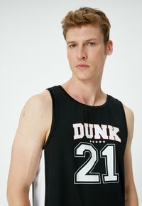 Sort basketballtrøje med et fremtrædende hvidt "21" og "DUNK" tekst i rød, med hvide sidelapper og en let stoftekstur.