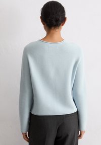 Jasnoniebieski sweter z dzianiny o okrągłym dekolcie, długich rękawach i luźnym kroju, zestawiony z ciemnymi spodniami w prążek. Miękka faktura.