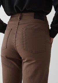 Bruine katoenen blend broek heeft achterzakken, een slim fit en zichtbare stiksels. De tailleband heeft een zwart leren patchdetail.