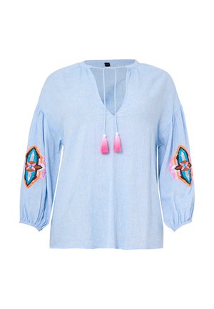 Himmelbluse aus Leinen mit V-Ausschnitt, zwei pinken Quasten und bestickten geometrischen Mustern an den Ärmeln in den Farben Pink, Blau und Braun.