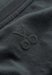 Donkergrijze stof met een gestructureerd schaarlogo in een bijpassende tint, vlakbij de halslijn geplaatst met ribbel-detail.