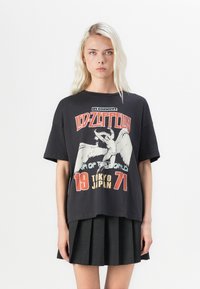 Black oversized t-shirt featuring a Led Zeppelin graphic print, with white and red accents, and short sleeves. Paired with a pleated black skirt.