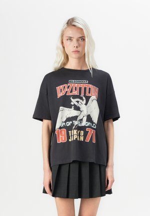 Black oversized t-shirt featuring a Led Zeppelin graphic print, with white and red accents, and short sleeves. Paired with a pleated black skirt.