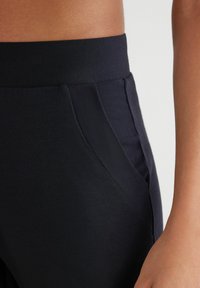 Zwarte sportbroek met een gladde textuur, voorzien van een brede tailleband en zijzakken. Close-up van de stiksels en pasvorm.