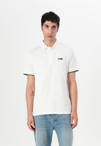 Witte katoen polo met zwarte accenten op de mouwen, met een klein geborduurd ontwerp op de linkerborst. Klassieke kraag en knoopsluiting.