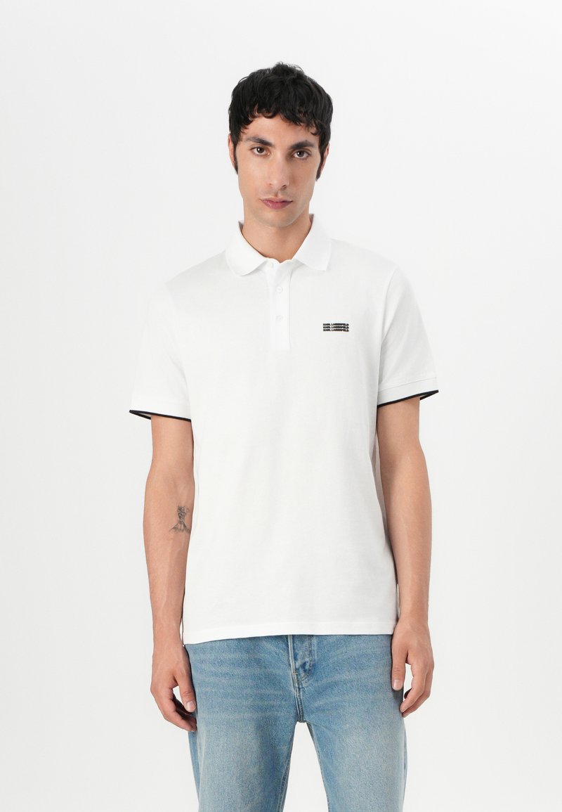 Witte katoen polo met zwarte accenten op de mouwen, met een klein geborduurd ontwerp op de linkerborst. Klassieke kraag en knoopsluiting.