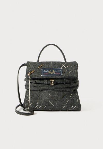 Sac à main en denim noir avec des coutures blanches décoratives, une poignée supérieure, une sangle réglable et une boucle en ton doré. Présente une étiquette de marque.