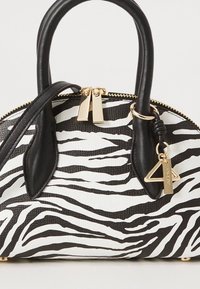 Veske med sebramønster i svart og hvitt imitert skinn, gullfarget metallbeslag, håndtak på toppen og avtagbar stropp. Pyntet med et trekantet anheng.