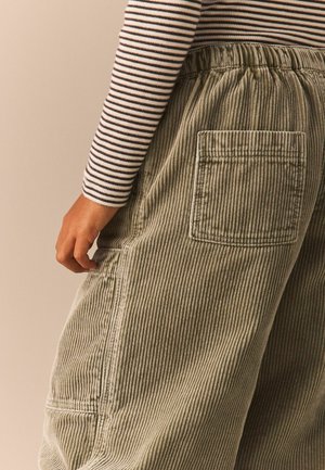 Pantalon en velours côtelé vert olive avec des rayures verticales, doté d'une taille élastique et d'une poche patch au dos. Détail de tissu texturé visible.