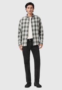 Šedá a bílá károvaná košile na knoflíky z bavlněné směsi, doplněná o černé džíny s rovnými nohavicemi a černé boty, vše vystaveno na neutrálním pozadí.