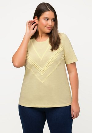 T-shirt gialla a maniche corte con un design a chevron stratificato e dettagli in pizzo. Realizzata in materiale morbido, presenta un colletto rotondo e una vestibilità rilassata.