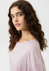 Haut à manches courtes rose clair avec une coupe décontractée. Tissu doux, encolure ronde et épaules légèrement tombantes créent un style décontracté.