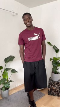 Maroon Puma t-shirt with white logo, paired with black shorts. Surrounded by plants and a grey rug on wooden flooring.