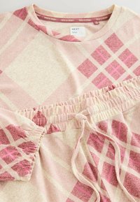 Rožinė ir kreminė langelių rašto laisvalaikio komplektas su apvaliu iškirpimu, elastinga juosmens juosta ir susiraukšlėtomis rankovėmis. Minkšta medžiaga su tekstūruotu paviršiumi.