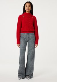 Rode gebreide trui met uitsparingen, getextureerde vlecht en lange mouwen, gecombineerd met hooggesneden, flared grijze jeans met patroon.