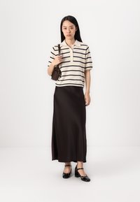 Randig krämfärgad pikée med korta ärmar, kombinerad med en lång, mörkbrun, satinkjol. Svarta klackskor fulländar outfiten.