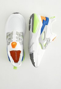 Hvide atletiske sneakers med en mesh-overdel, grå accenter og klare grønne, blå og orange detaljer. Tekstureret sål og logo på tungen.