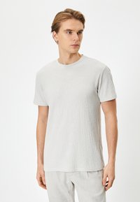 T-shirt grigio chiaro con texture, colletto a girocollo e maniche corte, realizzato in tessuto morbido. Motivo sottile visibile sulla superficie.