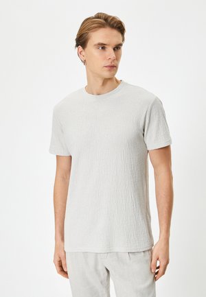 Camiseta de color gris claro texturizada con cuello redondo y mangas cortas, hecha de una tela suave. Patrón sutil visible en la superficie.