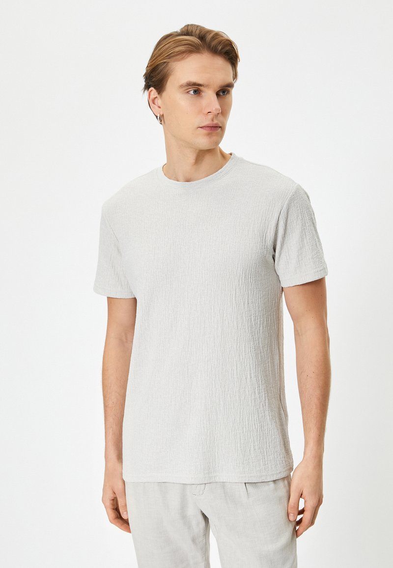 T-shirt grigio chiaro con texture, colletto a girocollo e maniche corte, realizzato in tessuto morbido. Motivo sottile visibile sulla superficie.