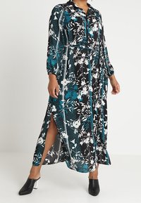 Lång svart klänning med blommönster i turquoise och vitt, knäppning med krage, långa ärmar och sidofickor. Mjukt, lätt tyg.