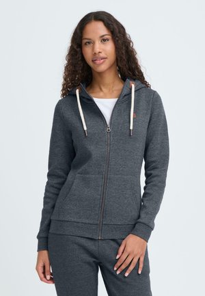 Grå hættetrøje med lynlås lavet af blødt stof, har en hætte med snøre, to forlommer og ribbede manchetter. Brune detaljer ved lynlåsen.