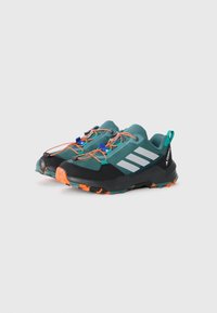 Ein Paar türkisfarbene und schwarze Trailrunning-Schuhe mit orangen Schnürsenkeln und Sohlen, die drei weiße Streifen und eine strukturierte Profilsohle aufweisen.