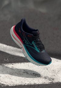 Laufschuh mit schwarzem strukturiertem Obermaterial, türkisen Akzenten, pinkem Absatz und dicker weißer Sohle. Verfügt über ein Schnürdesign und Logodetails.