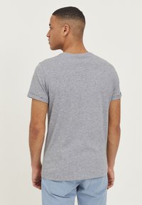 Tricou gri cu mânecă scurtă, cu gât rotund, fabricat dintr-un amestec de bumbac, având manșete rulate și o etichetă discretă a brandului pe mânecă.