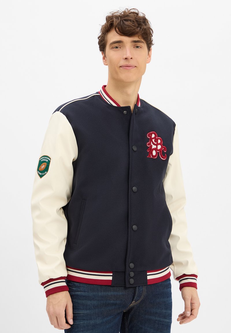 Marineblaue Collegejacke mit cremefarbenen Ärmeln, rot-weißer gestreifter Rippkragen und Bündchen sowie gesticktem "RBC"-Logo. Verfügt über Seiten pockets.