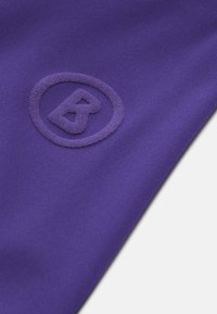 Lilla tekstil med en blød tekstur og et forhøjet, cirkulært logo med et stiliseret bogstav "B" i midten.