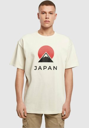 Kremfarget bomull T-skjorte med et rødt sol, svart fjellgrafikk, og ordet "JAPAN" i fet svart tekst under designet.