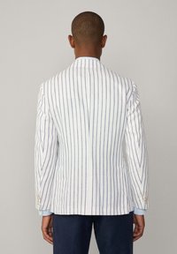 Blazer en lin blanc avec des rayures verticales bleues, fente simple au dos et poignets boutonnés. Texture douce et coupe ajustée.