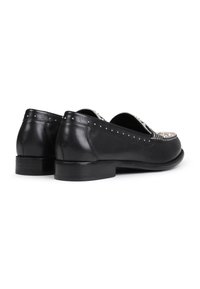 Mocasines de cuero negro con un tacón bajo, que cuentan con tachuelas decorativas plateadas a lo largo del borde superior y una textura suave.