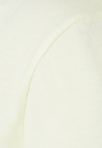 Tessuto giallo chiaro con una superficie liscia e un sottile motivo a righe. Presenta cuciture curve e una finitura morbida.