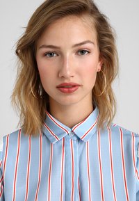 Light blue button-up shirt with red and white vertical stripes; cotton fabric; features a collar and two lace accents on shoulders.