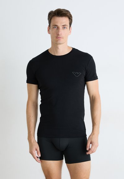 T-shirt noir à manches courtes en tissu doux, avec un logo discret sur la poitrine. Assorti à un slip noir ajusté.