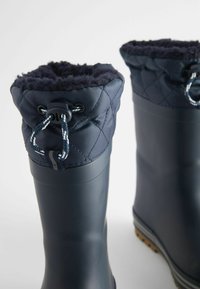 Bottes en caoutchouc navy avec un col en nylon matelassé, doublure en fourrure en haut et fermeture à cordon. Semelle texturée offrant une bonne traction.