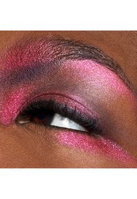 Nærbillede af et øje med dristig, glitrende pink øjenskygge og veldefinerede vipper på mørk hud. Øjenlåget har en gradient-effekt med mørkere nuancer.