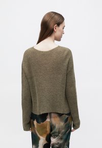 Pulover tricotat verde măsliniu, cu decolteu lat rotund și mâneci lungi. Spatele are o margine ușor rotunjită și o textură moale.