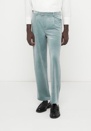 Calças de veludo numa tonalidade azul clara com uma textura suave, apresentando um ajuste ajustado, duas pregas à frente e bolsos laterais.