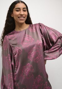 Satinlångärmad topp i dämpad mauve med stort rosa blommönster och texturerade detaljer, med puffärmar och rund halslinning.