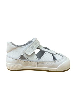 Zapato infantil de cuero sintético blanco con diseño recortado, correa de Velcro, suela de goma y detalles texturizados a lo largo de los bordes.