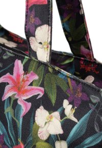 Stoffen draagtas met een zwarte achtergrond, voorzien van een kleurrijk bloemenpatroon met roze lelies en witte orchideeën. Dubbele handvatten zijn zichtbaar.