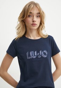 T-shirt in cotone blu navy con un brillante logo grafico "LIU JO MILANO" in tonalità bianche e argentate, con scollo rotondo e maniche corte.