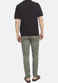 Polo shirt noir à manches courtes associé à un pantalon slim-fit vert clair en tissu à finition mate et des chaussures brunes à enfiler. Design simple, sans motifs.